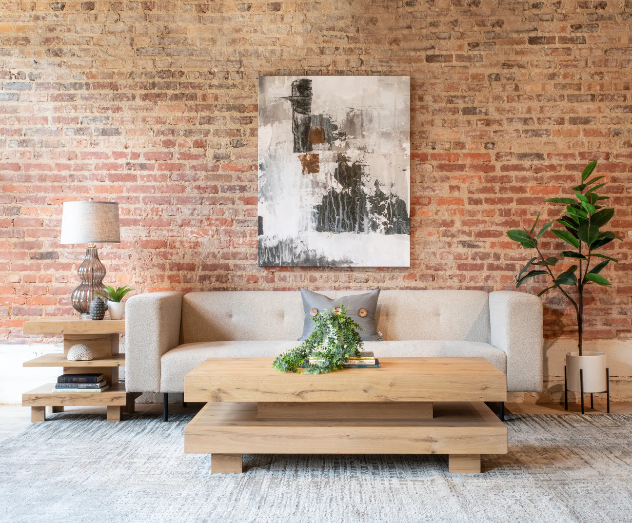 sample living room with coffee and side table, sofa, plant and abstract painting on brick wall