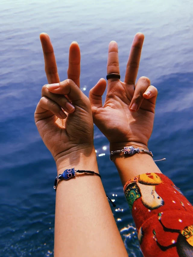two girls' wrists showing off their beaded bracelets over water
