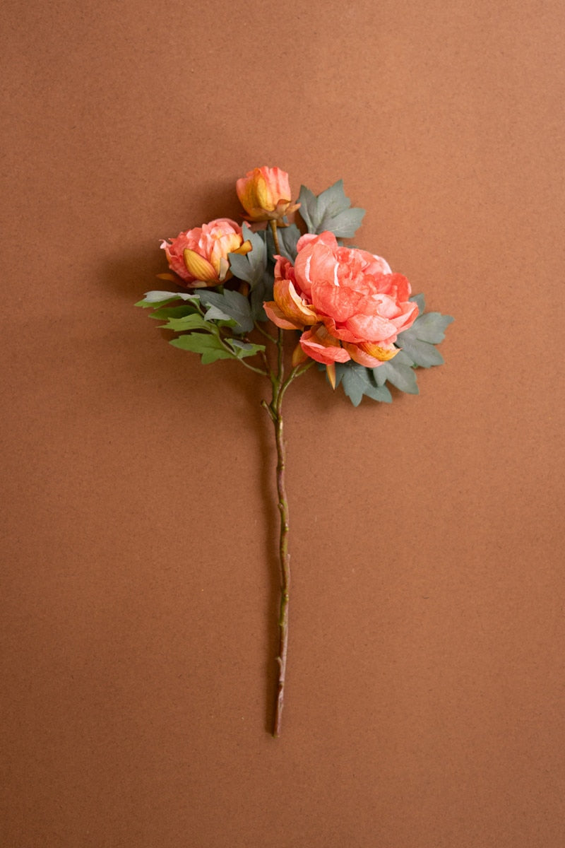 Artificial flower arrangement of long stem coral color peonies against a brown background