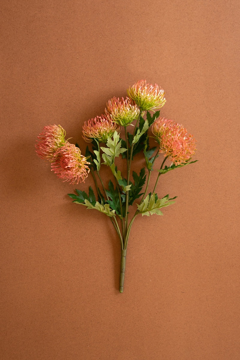 A bouquet of artificial orange and green flowers with green leaves on a solid brown background.