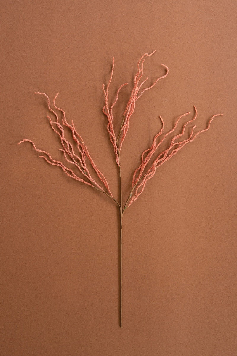 A single dried decorative branch with a thin brown stem and many fine coral-pink twigs branching from the top, centered on a warm brown background.