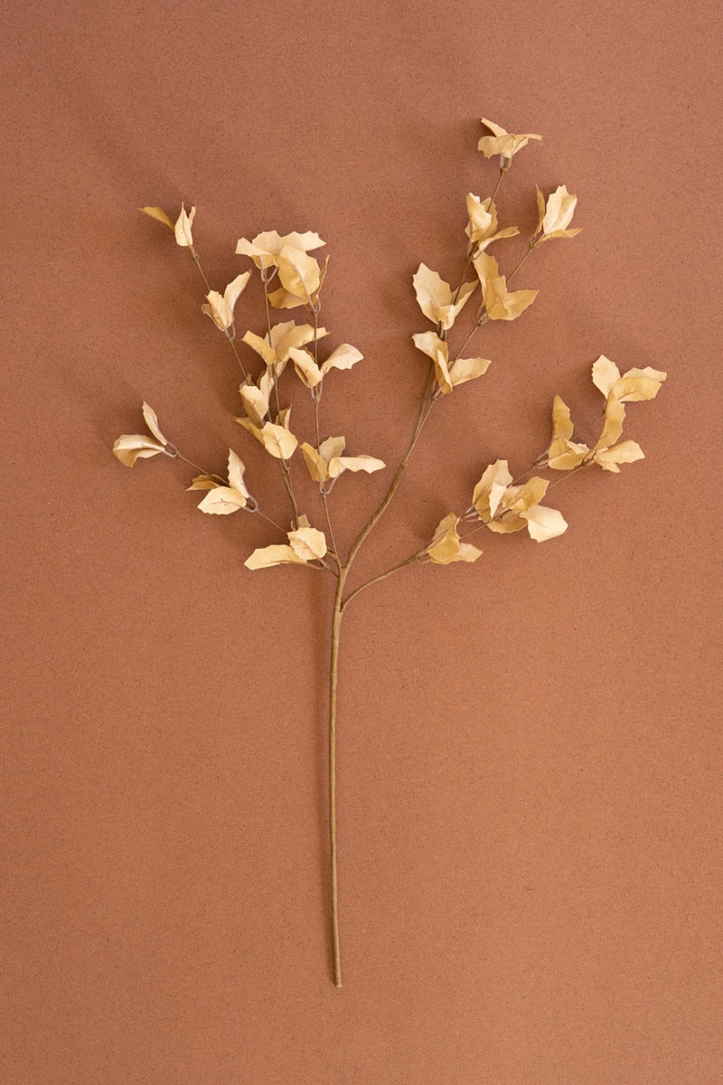 A dried decorative branch with small pale beige leaves on a long stem, photographed against a solid warm brown background