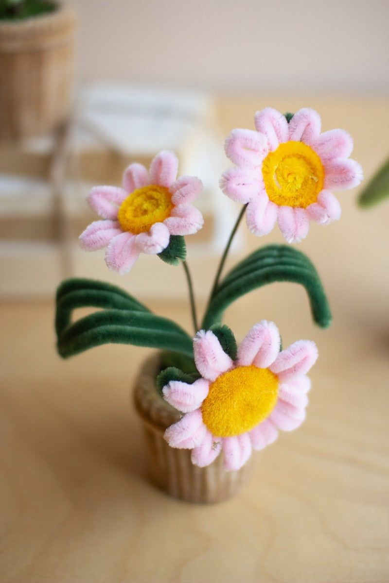 Knitted flowers with pink petals and yellow centers in a small pot on a wooden surface.