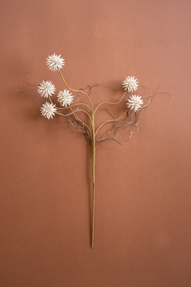 A faux dried floral wall sculpture featuring five white starburst flowers on branching tan and brown stems, displayed against a solid terracotta background.
