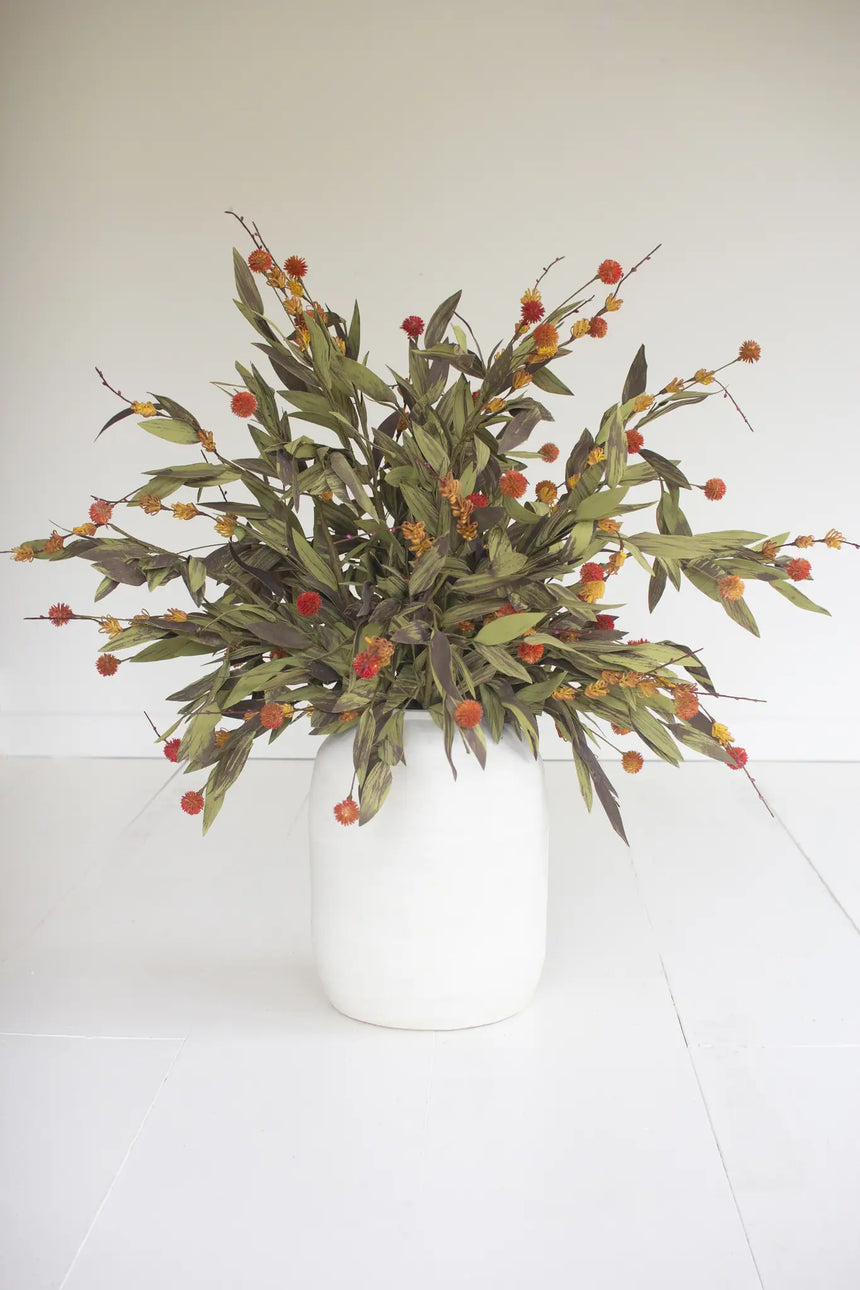 A dried floral arrangement featuring olive green leaves and clusters of small orange-red berries, presented in a matte white ceramic vase against a clean white background.