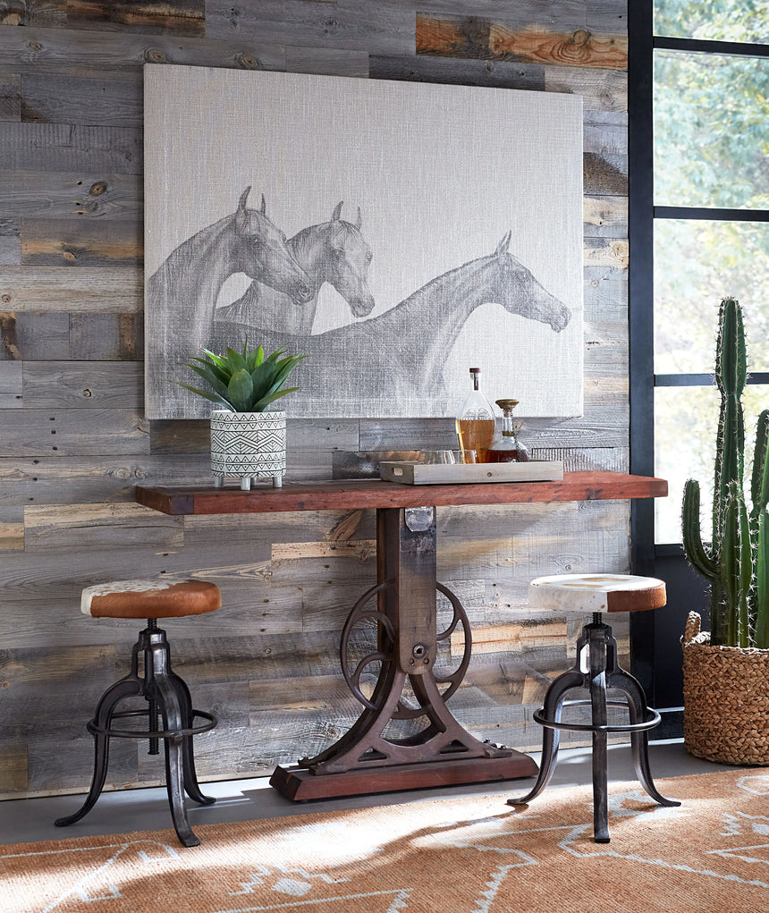 Sterling 56in Console Table in Cast Iron and Teak Wood in home setting shown with bar stools and cactus and wood panel wall in background