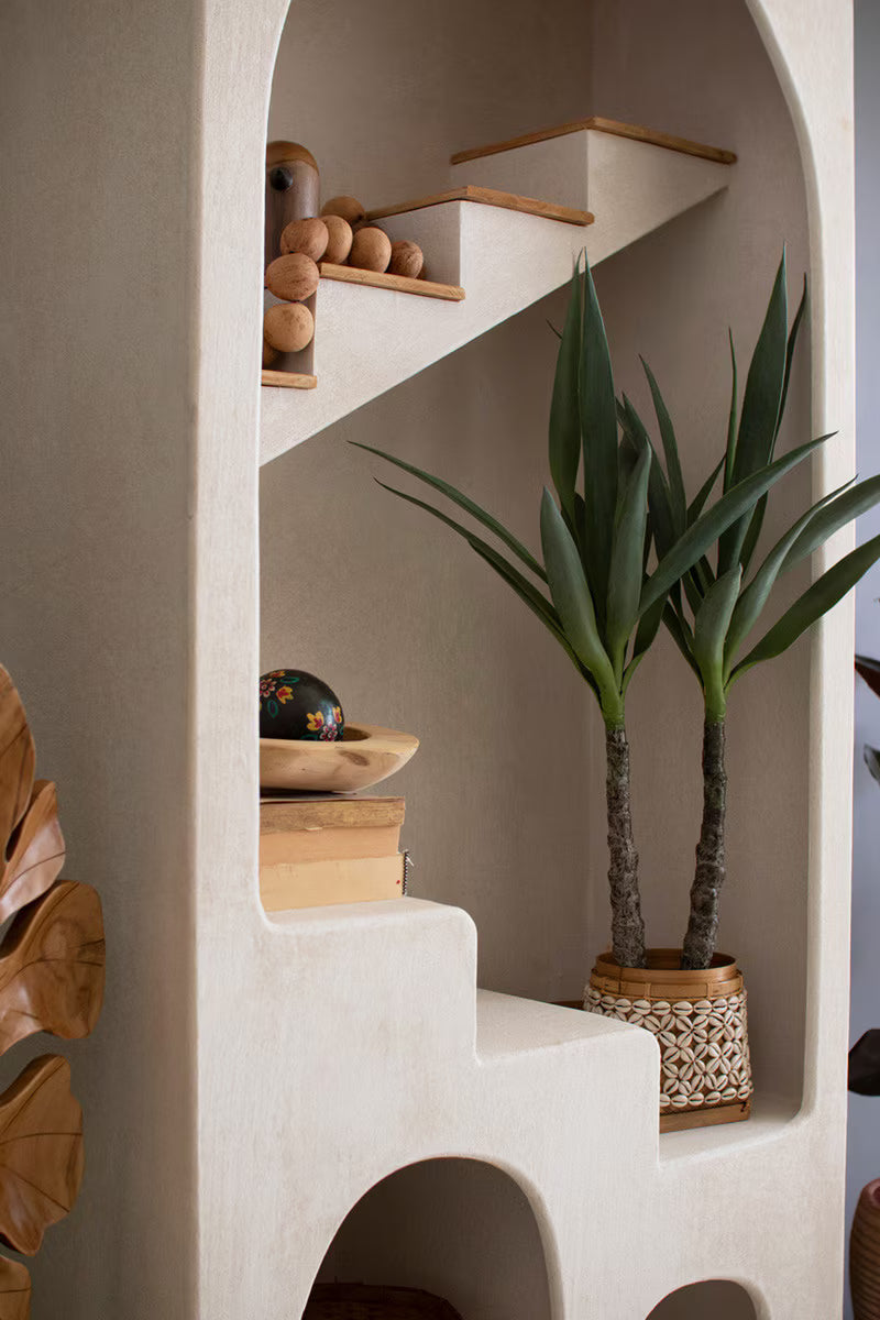 Decorative interior with white plaster shelf with arch design and steps detail showing plants, books and sculptures