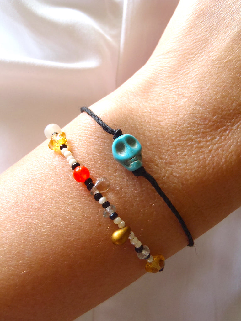 set of bracelets, one with black cotton thread, the other with multicolored seed and glass beads shown on a lady's wrist