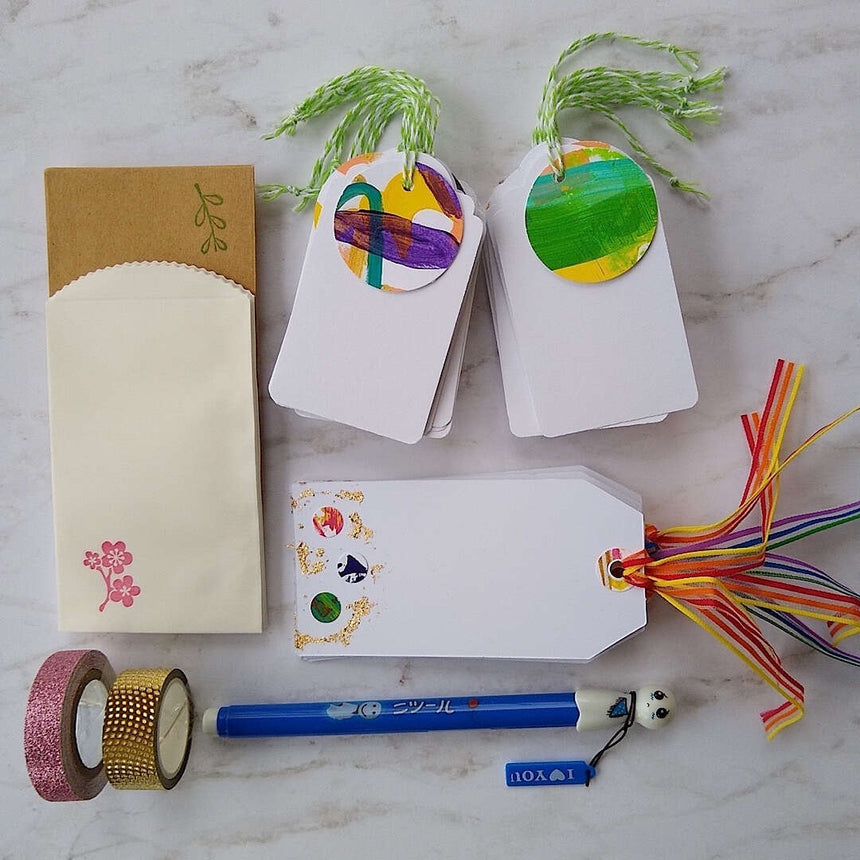 abstract confetti and gold foil gift tags, white gift tags, mini envelopes, Japanese doll pen, Japanese washi tape, laid out on a table