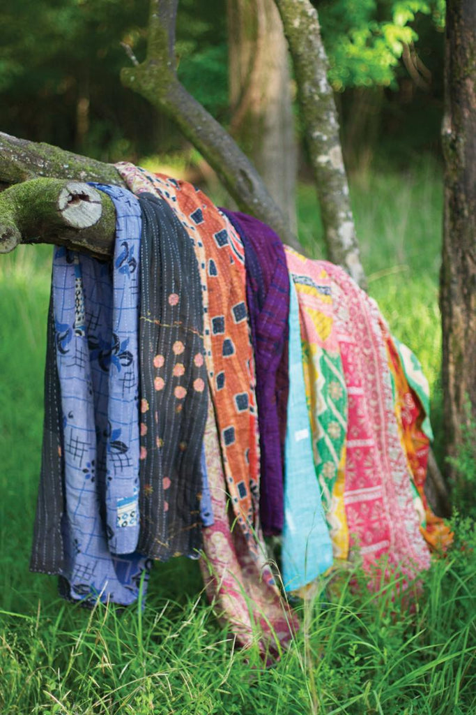 several kantha throws of different colors hung over a tree branch
