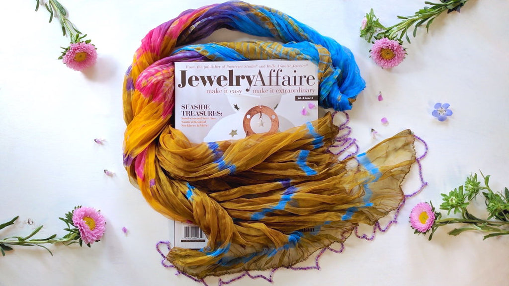 Colorful silk scarf framing Jewelry Affair magazine with featured article