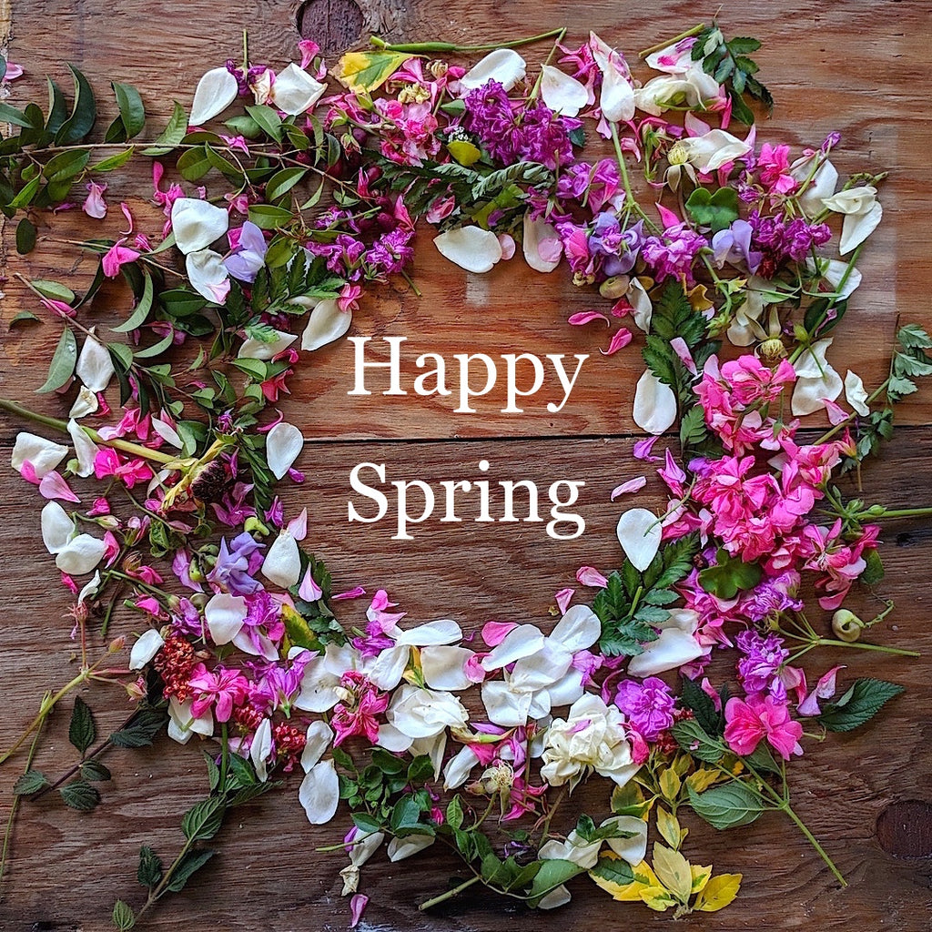 Wreath of flowers on dark wood background labeled "Happy Spring"