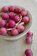 string of purple faux onions - shown in a bowl with some faux onions on the table