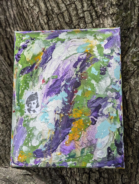 Original colorful abstract painting on a textured surface shown propped up on a tree as background