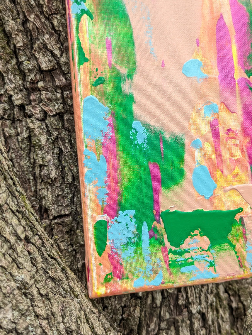 Colorful abstract painting leaning against a tree trunk with focus on lower left corner