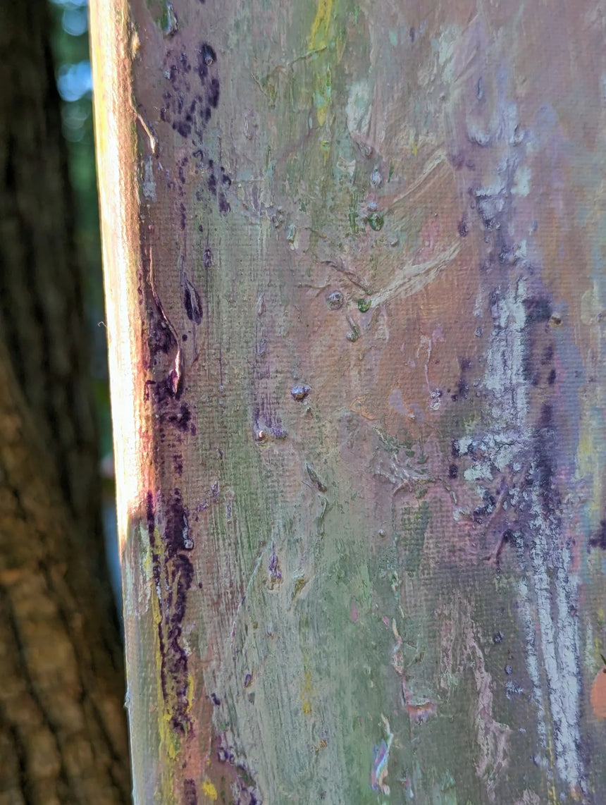 A close-up of a textured canvas or print showing layered paint strokes in muted green, brown, beige, and purple tones, with a blurred tree trunk visible on the left edge against the sunlight.