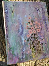 An abstract floral canvas painting tilted against a tree trunk while being lit up by golden sunlight.