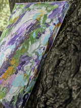 Colorful abstract painting leaning against a tree trunk seen from a side angle