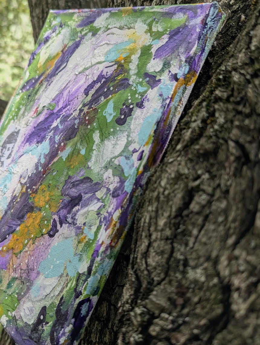 Colorful abstract painting leaning against a tree trunk seen from a side angle