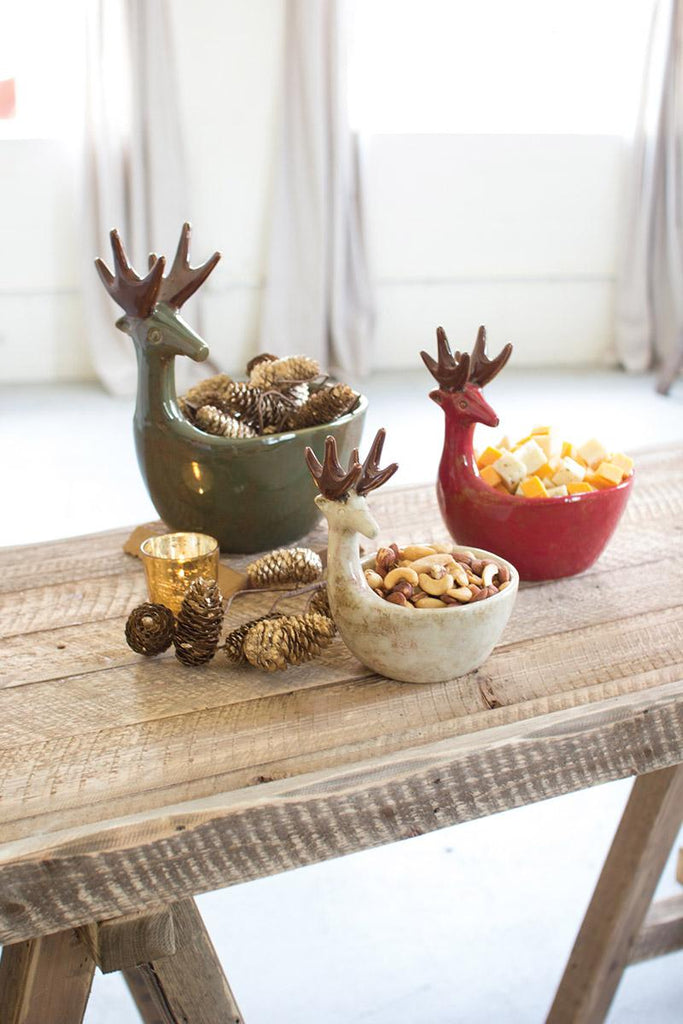 set of 3 ceramic deer bowls in green, red and off-white colors on wooden table filled with snacks