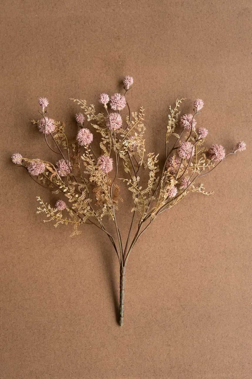 Artificial flower arrangement with pink and gold elements on a brown background