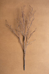 A single artificial-looking bare twig branch with many thin branches extending upward, photographed against a plain warm tan background.