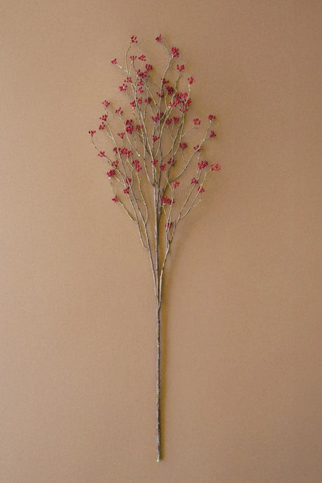 A single artificial floral stem with thin brown branches and small pink blossoms, photographed against a plain warm beige background