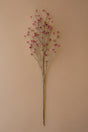 A single artificial floral stem with thin brown branches and small pink blossoms, photographed against a plain warm beige background