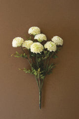 A bouquet of artificial white dalhia flowers with green stems and leaves, arranged against a solid brown background
