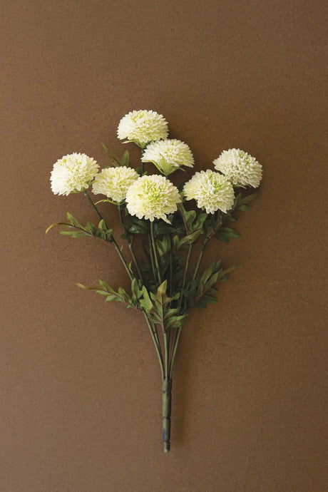 A bouquet of artificial white dalhia flowers with green stems and leaves, arranged against a solid brown background