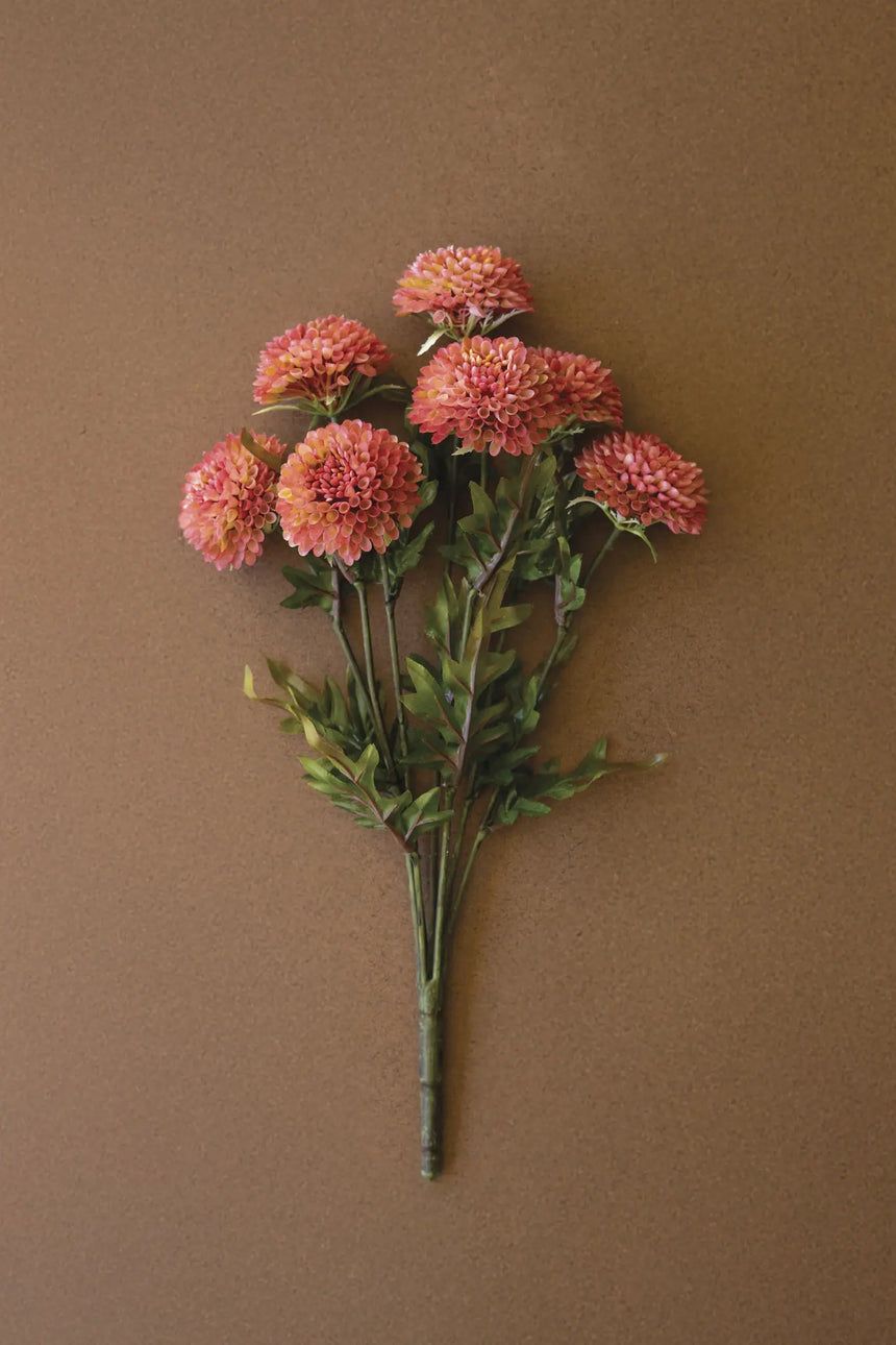 A bouquet of artificial faux pink dalhia flowers with green stems and leaves, arranged against a solid brown background