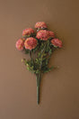 A bouquet of artificial faux pink dalhia flowers with green stems and leaves, arranged against a solid brown background