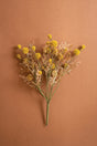 A faux dried flower bouquet with small yellow globes and pale beige filler stems on a plain warm brown background