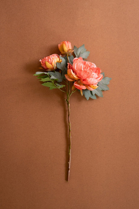 Artificial flower arrangement of long stem coral color peonies against a brown background