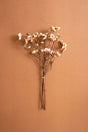 A small bouquet of artificial peach blossom branches with pale pink flowers and brown stems, tied with a thin band and displayed against a solid warm brown background.