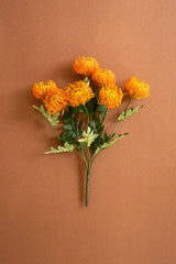 A bouquet of artificial orange protea with green leaves and stems, arranged on a solid brown background.