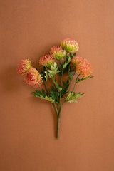 A bouquet of artificial orange and green flowers with green leaves on a solid brown background.