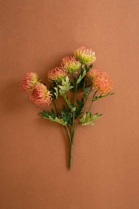 A bouquet of artificial orange and green flowers with green leaves on a solid brown background.