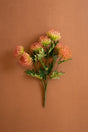 A bouquet of artificial orange and green flowers with green leaves on a solid brown background.