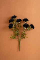 An artificial flower stem bouquet with six dark black globe-shaped blooms, green leaves, and a single long stem, arranged on a solid warm brown background