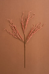 A single dried decorative branch with a thin brown stem and many fine coral-pink twigs branching from the top, centered on a warm brown background.