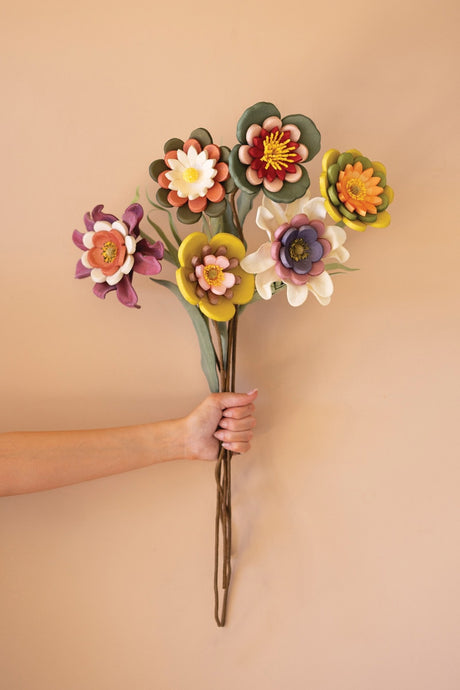 Hand holding a bouquet of colorful artificial, foam flowers against a beige background