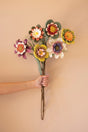 Hand holding a bouquet of colorful artificial, foam flowers against a beige background