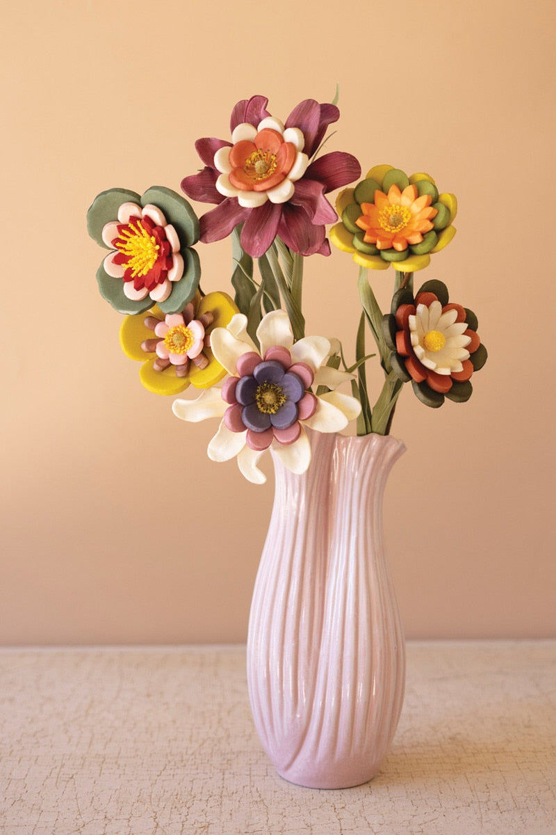 Pink vase with colorful artificial flowers against a beige background