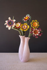 A pink ribbed ceramic vase holding a bouquet of colorful handmade eva foam flowers, set against a dark gray background and a light textured tabletop.