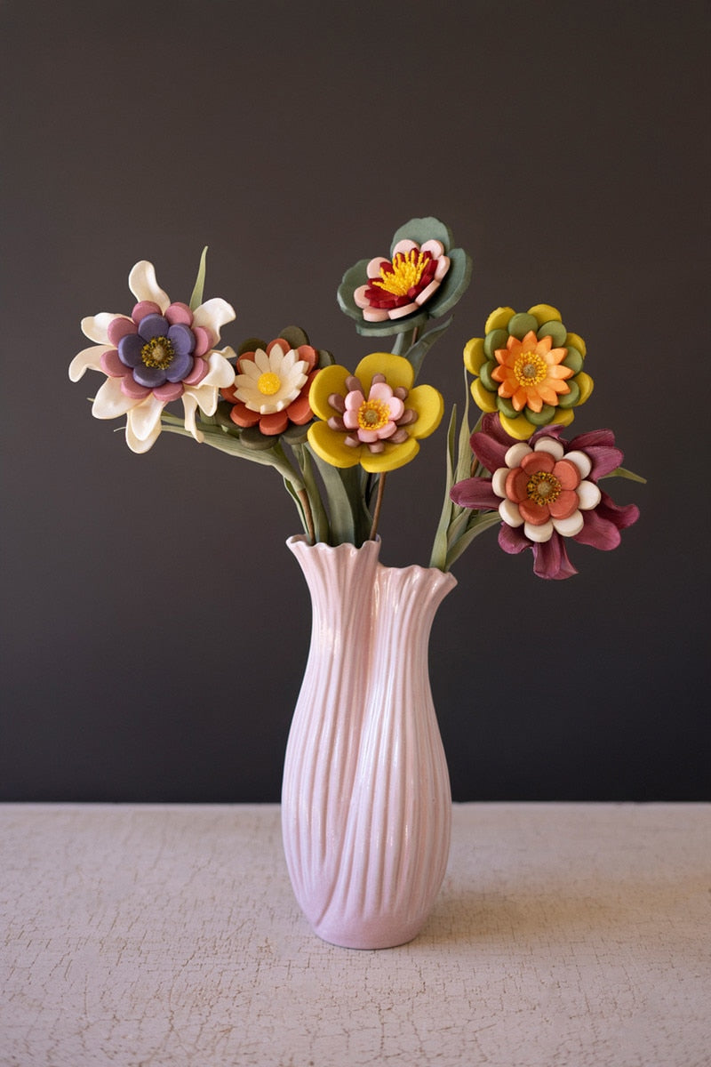 A pink ribbed ceramic vase holding a bouquet of colorful handmade eva foam flowers, set against a dark gray background and a light textured tabletop.