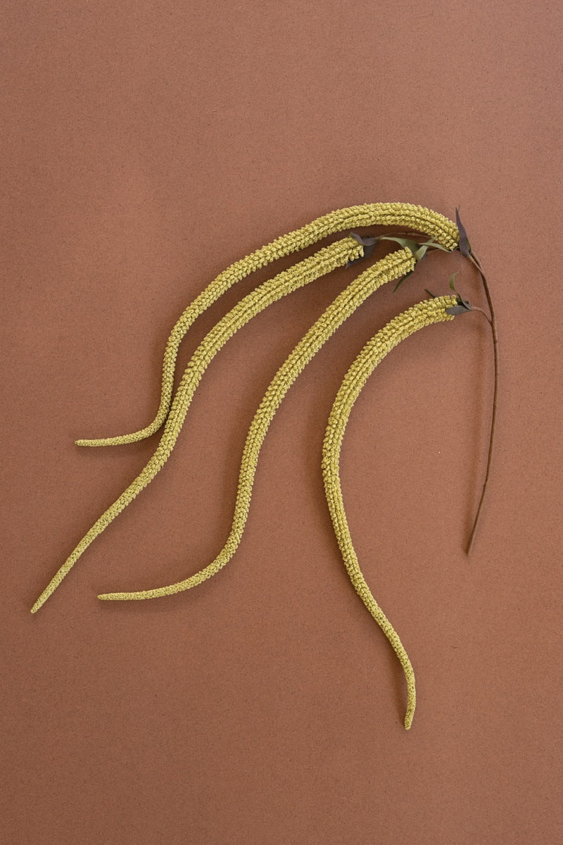 Yellow faux amaranthus plant stems against a brown background