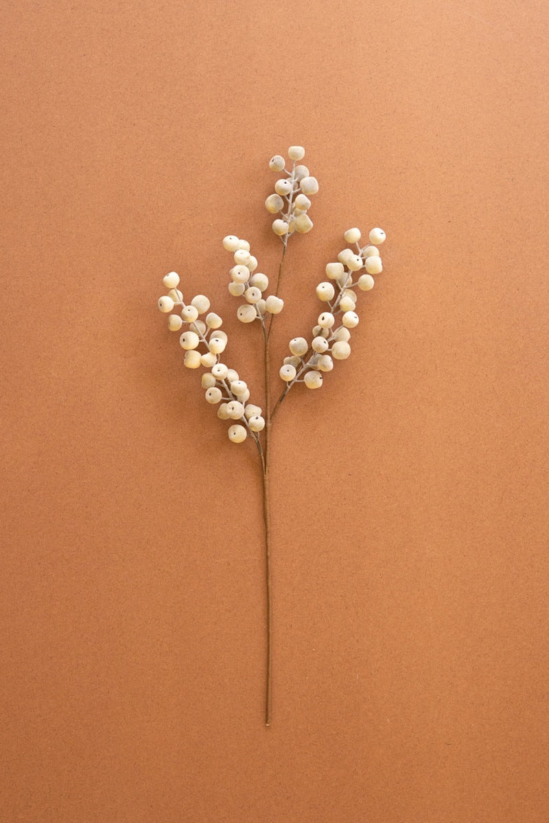 A decorative faux floral stem with clusters of small off-white pearl-like berries on a thin brown stem, photographed against a solid warm terracotta background.