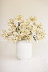 A bouquet of cream-colored artificial magnolia flowers arranged in a matte white ceramic vase, set against a clean, off-white background.