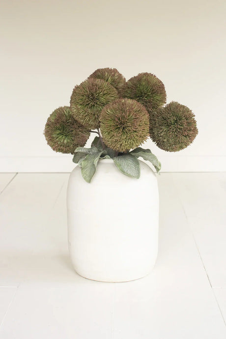 White vase with green decorative balls on a white surface